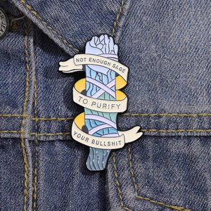Détail d'un pin's créatif en émail sauge avec message sur un col de veste en jean