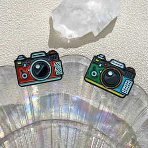 Retro camera enamel pins in red, blue and yellow on an iridescent shell tray