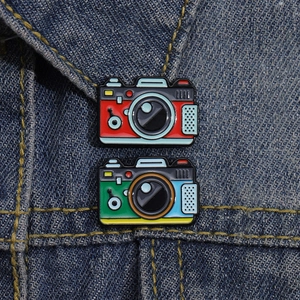 Retro vintage camera enamel pins in colorful alloy sets on dark denim fabric