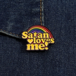 Nahaufnahme der Satan Loves Me Emaille-Regenbogennadel auf blauem Denim-Stoff