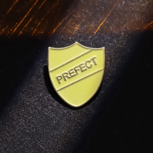 Macro shot of yellow shield-shaped metal pin with PREFECT engraving on dark background