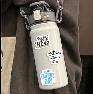 Close-up of white stainless steel water bottle with Father's Day hero stickers and gray strap