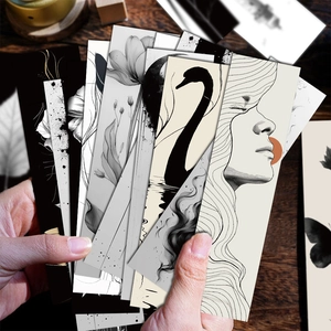 Artistic black and white bookmarks with ink illustrations held over dark wooden desk