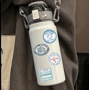 Close-up of a white sports water bottle with vintage travel stickers and carry strap