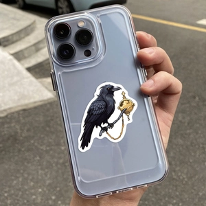 Close-up of a clear phone case with a fantasy black raven design held by hand outdoors