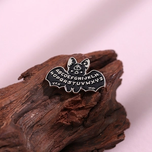 Spilla gotica a pipistrello in smalto nero con design alfabeto Ouija su fondo in legno