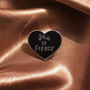Geometric heart-shaped enamel brooch with She IS FIERCE text on brown silk background
