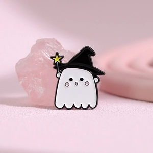Detail of cute ghost enamel pin with witch hat and magic wand on pink crystal background