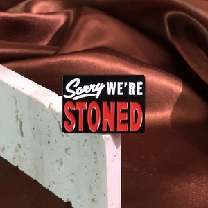 Rectangular 'Sorry We're Stoned' enamel pin badge on stone and brown satin fabric