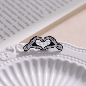 Broche cœur mains squelettes en émail noir sur une assiette décorative blanche