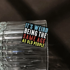 Close-up of a square enamel pin with It's Weird Being The Same Age As Old People quote
