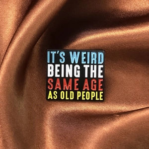 Detail of square enamel pin with colorful quotes on a premium brown silk background