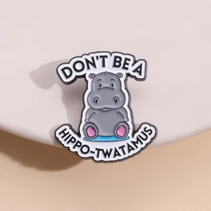 Funny enamel hippo brooch with humorous English text on a clean ceramic display