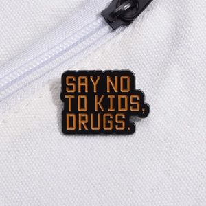 Creative black enamel pin with orange text saying SAY NO TO KIDS DRUGS on canvas bag