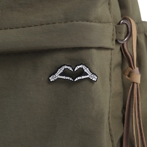 Détail macro d'un pin's émaillé mains de squelette formant un cœur sur tissu vert olive