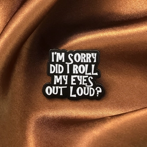 Detail of black enamel pin with white text 'I'M SORRY DID I ROLL MY EYES OUT LOUD?'