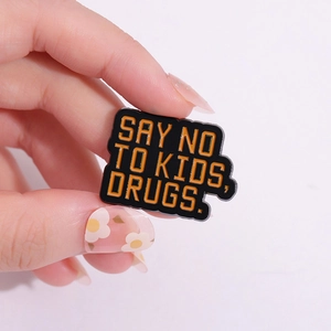 Funny enamel pin featuring 'SAY NO TO KIDS, DRUGS' text on black alloy badge