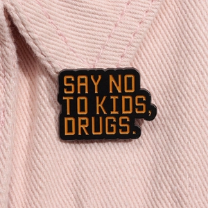 Detail of enamel pin with 'SAY NO TO DRUGS' text pinned on pink denim fabric