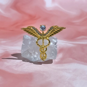 Macro shot of a golden Caduceus medical brooch with light blue stone and small rhinestones