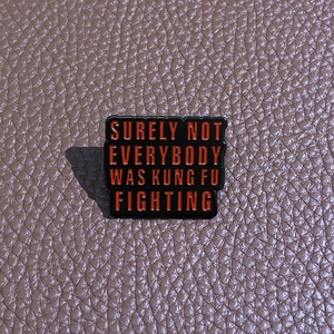 Close-up of rectangle enamel pin with humorous text on a brown leather surface