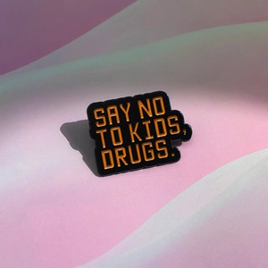 Black enamel pin with orange Say No to Kids Drugs slogan on purple background