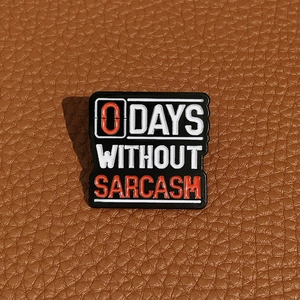 Macro detail of '0 DAYS WITHOUT SARCASM' enamel pin on brown leather background