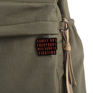 Detail of creative metal enamel pin with quote on a green nylon backpack texture