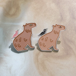 Charming capybara enamel pins with cute birds on a textured stone surface display