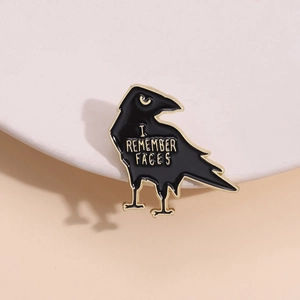 Detail of raven brooch featuring I REMEMBER FACES text in gold engraved finish