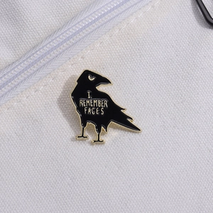 Creative black enamel crow brooch with I REMEMBER FACES text on white canvas