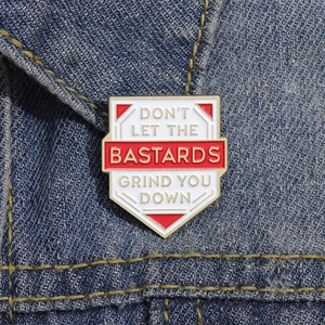 Close-up of shield enamel pin with motivational text pinned on blue denim jacket