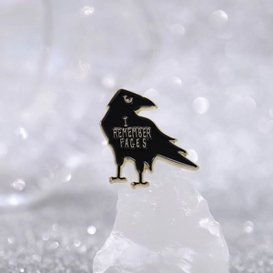Creative black raven enamel pin with I REMEMBER FACES text on a white mineral stone