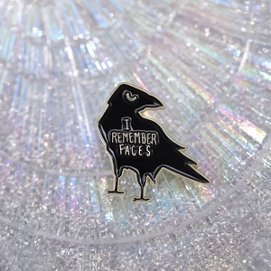 Black crow enamel pin with I REMEMBER FACES text and golden metal finish details