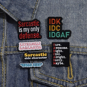 Close-up of six enamel pin badges with sarcastic slogans on denim jacket fabric