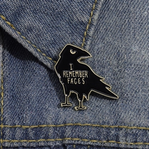 Creative black crow enamel pin with I REMEMBER FACES text on blue denim fabric