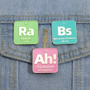 Three creative science enamel pins with chemical element symbols on blue denim jacket pocket