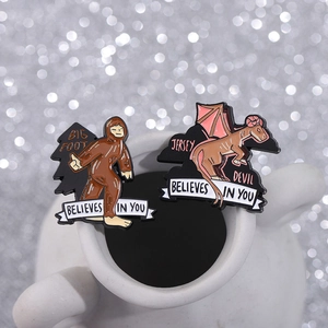 Bigfoot and Jersey Devil enamel pins with Believes in You text on a white mug rim