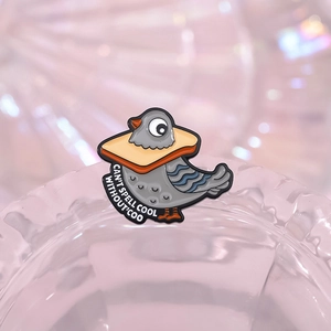 Enamel pigeon breadcrusting pin with 'COO' text detail on a glass edge macro view