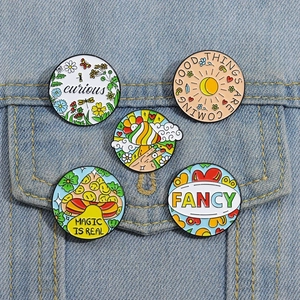 Detailed close-up of 5 enamel pins with inspirational slogans on denim jacket pocket