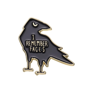 Black crow alloy enamel pin with gold 'I REMEMBER FACES' text on a white background