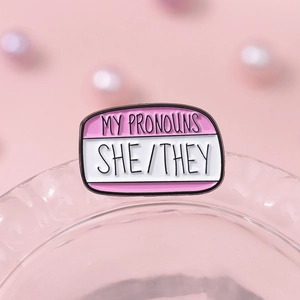Pink enamel pin featuring She/They pronouns in a speech bubble style on glass rim