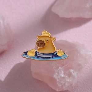 Cute capybara enamel pin with yellow ducks in blue water on a pink stone background