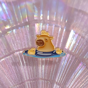 Cute cartoon capybara enamel pin with yellow duckling swimming in blue water ripples