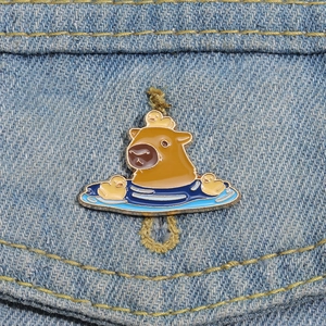Cute capybara and duck enamel pin badge accessory displayed on a blue denim jacket pocket