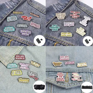 Set of colorful enamel pins with motivational quotes displayed on blue denim fabric