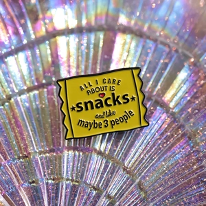 Yellow snack bag enamel pin with 'All I care about is snacks' funny quote badge