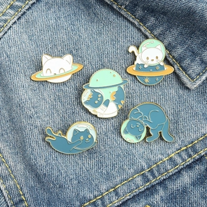 Detailed view of five space-themed cat enamel pins on blue denim fabric texture