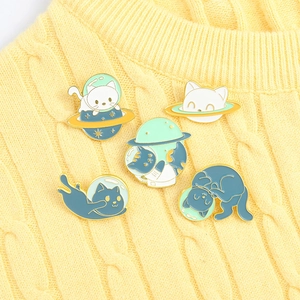 Detailed close-up of cute space cat enamel pins displayed on a yellow knit sweater