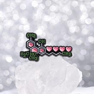 Dettaglio di spilla smaltata con cuore rosa e struttura molecolare chimica su cristallo