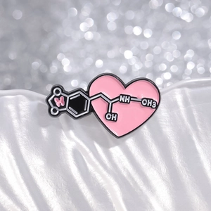 Vista macro di una spilla smaltata a cuore rosa con formule chimiche su tessuto bianco